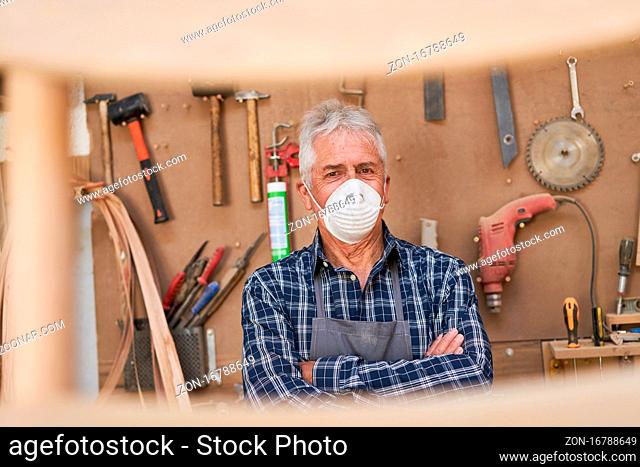 Handwerker Meister mit Maske wegen Covid-19 in seiner Werkstatt mit viel Werkzeug