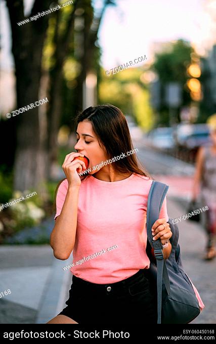 Portrait of a young woman biting apple against a street background