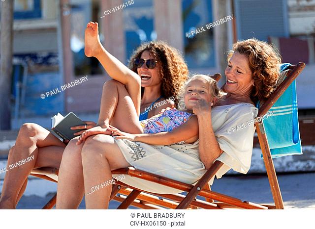 Playful, happy multi-generation women relaxing on sunny beach