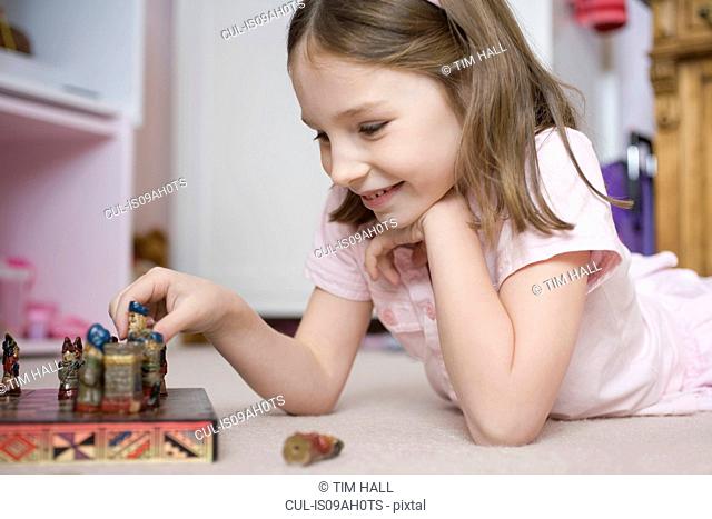 Young girl lying on bedroom floor playing with chess set