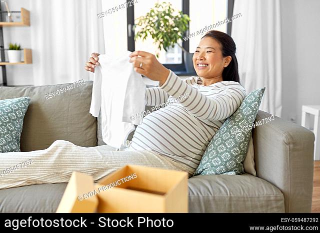 happy pregnant woman with baby's bodysuit at home