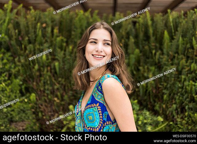 Smiling young woman in front of green shrub