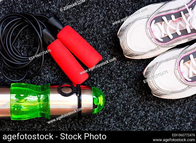 Sneakers, skipping rope and bottle of water on a dark background