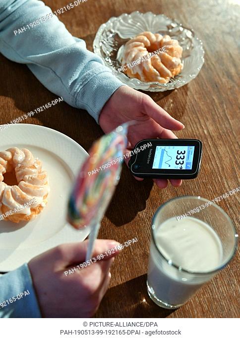 28 February 2019, Berlin: ILLUSTRATION - A girl is holding a Freestyle Libre blood glucose meter with far too high a blood glucose level next to plates of cake