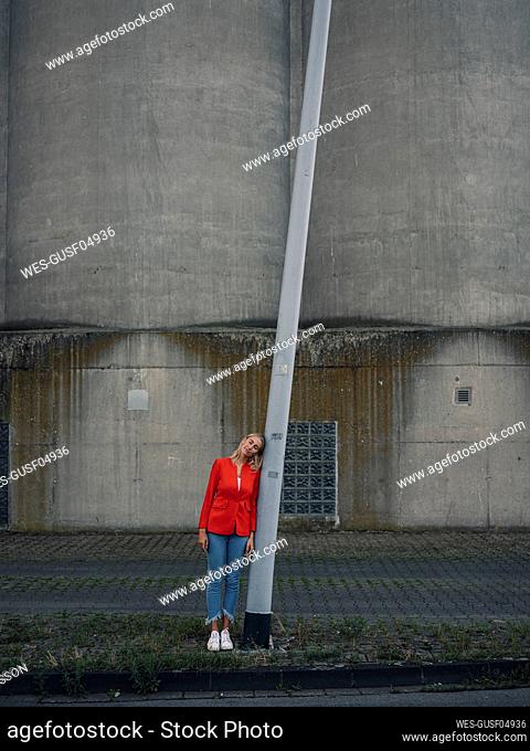 Female entrepreneur leaning on pole while standing against industry