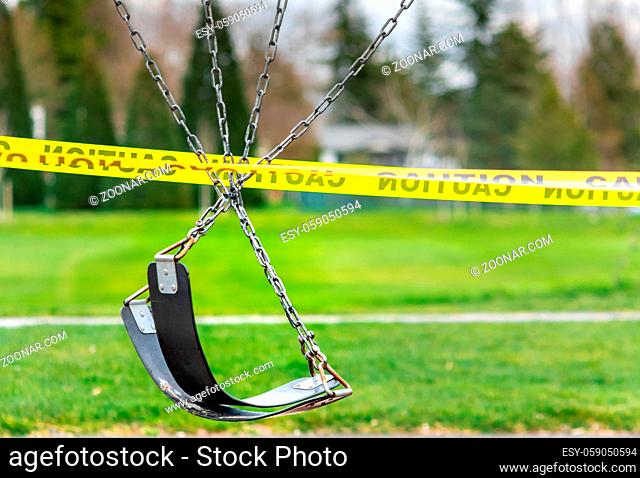 Black rubber swings on chains in closed public playground surrounded by yellow caution tape during time of Corvid-19 Coronavirus pandemic