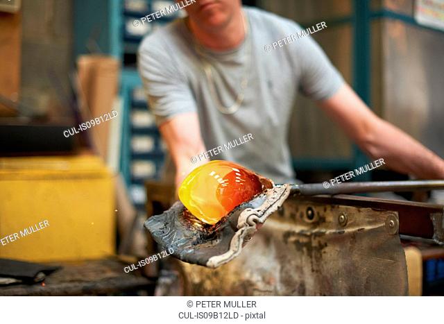 Glassblower in workshop forming molten glass on blowpipe