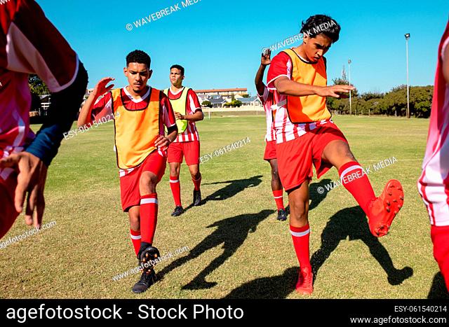 Male multiracial athletes stretching legs while exercising on playground against clear sky in summer