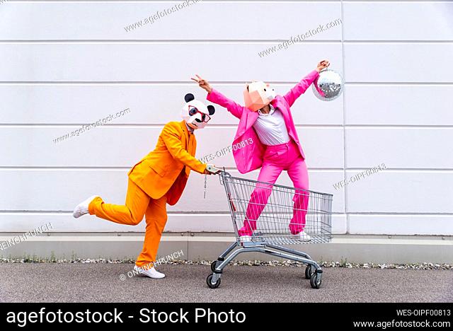 Man and woman wearing vibrant suits and animal masks¶ÿmessing around with shopping cart and disco ball