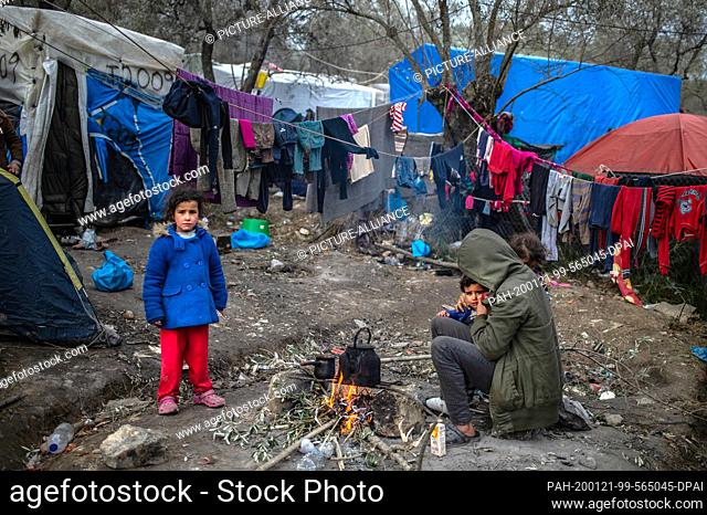 21 January 2020, Greece, Lesbos: A migrant family is trying to warm themselves by a small fire in a temporary camp next to the camp in Moria