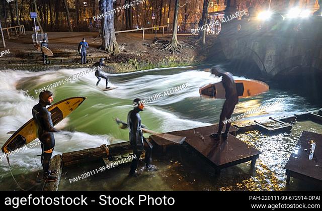 11 January 2022, Bavaria, Munich: A man surfs in wintry temperatures in the late evening on the artificial wave of the Eisbach in the English Garden in the...