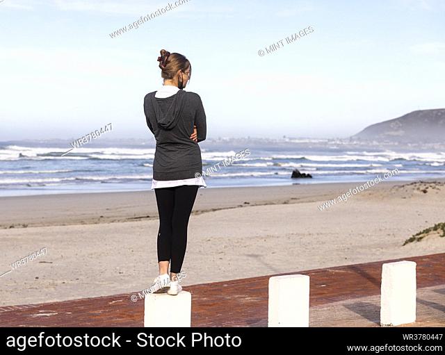 A teenage girl balancing on posts on a sandy beach