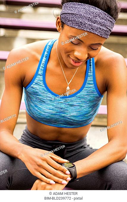 Black woman sitting on bleachers checking smart watch