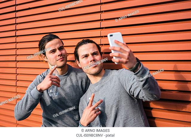 Young adult male twins taking a training break, taking selfie
