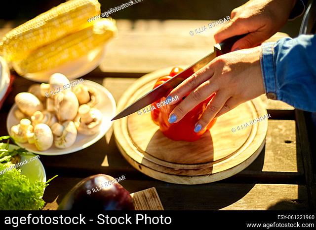 Unrecognizable woman cutting fresh pepper vegetables on wooden board during weekend barbecue in yard, outdoor, prepare for grilling, summer family picnic
