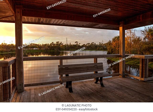 Sunset Wooden bench on a secluded, tranquil boardwalk along a marsh pond in Freedom Park in Naples, Florida