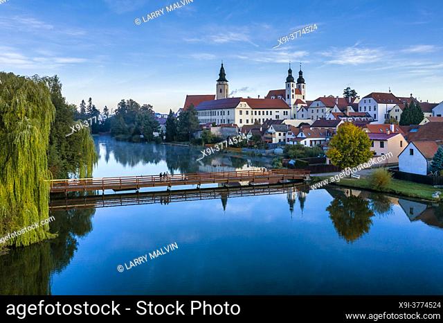 Aerial view before sunrise with three photographers on a bridge in front of the Telc Castle with foreground pond and castle reflections in the Czech Republic