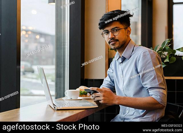 Freelancer with smart phone and laptop sitting in cafe