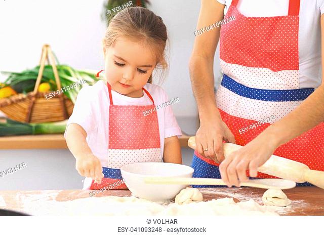 Mother and her cute daughter prepares the dough at wooden table. Homemade pastry for bread or pizza. Bakery background