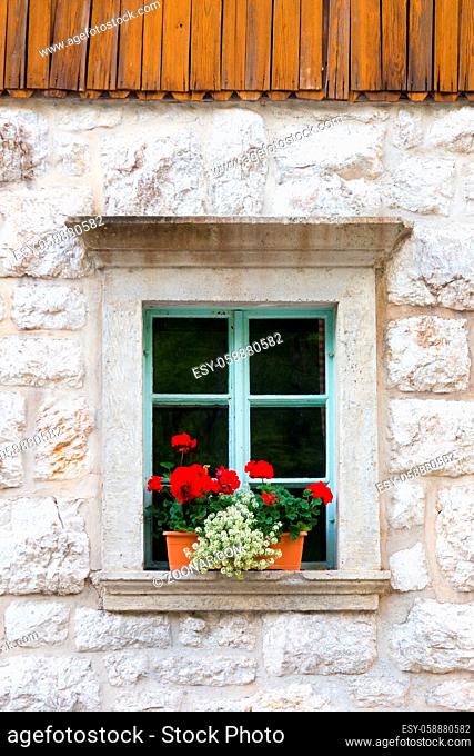 Vintagel alpine stone window with typical red carnation flowers on window sill. Detail from traditional mountain house with wooden paneling