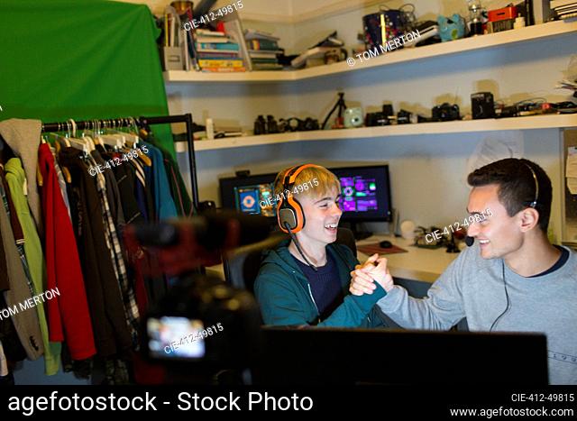 Happy teenage boys with headsets playing video game at computer in bedroom