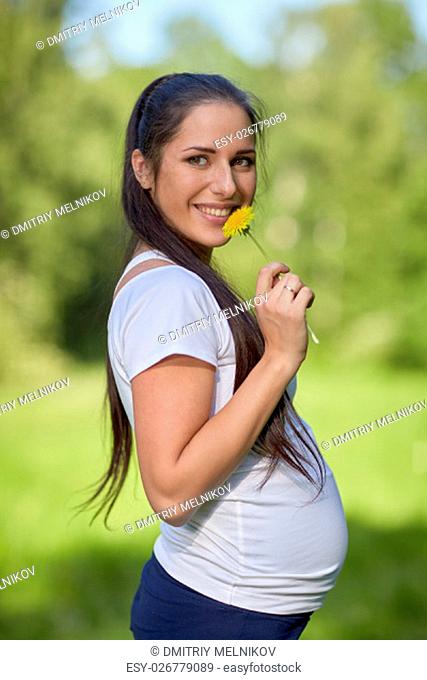 Young pregnant woman with flower in the summer park