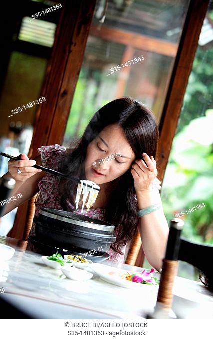 A young woman in a restaurant having 'guoqiao mi xian' (Crossing the bridge noodles) a kind of rice noodle soup from Yunnan, Kunming, China
