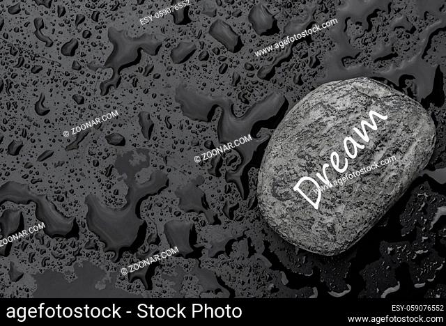 Conceptual image with the word dream written on a stone, on a black background sprinkled with rain droplets