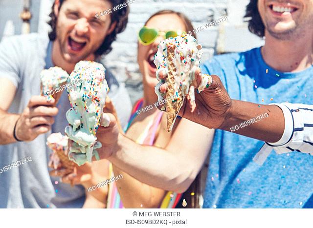 Young woman and men holding up melting ice cream cones, laughing