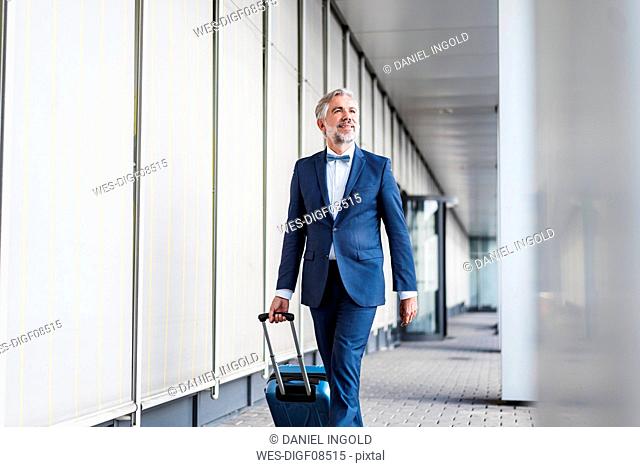Mature businessman in a passageway with rolling suitcase on the go