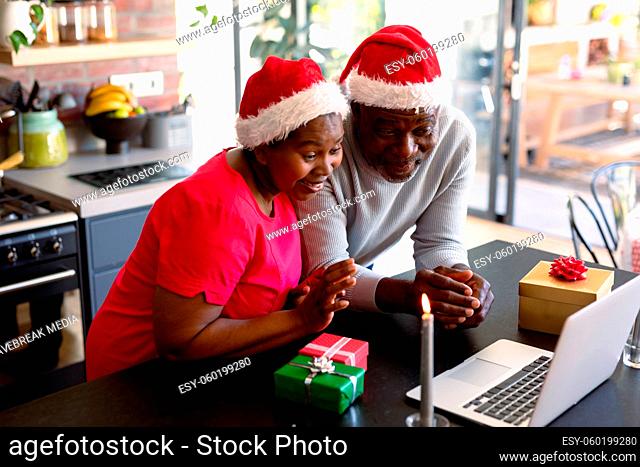 Happy african american senior couple having video call on laptop in kitchen at christmas time