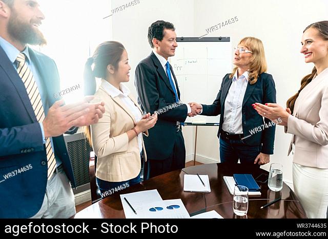 Two middle-aged business managers shaking hands as a gesture of congratulations for success and achievement during meeting in the conference room