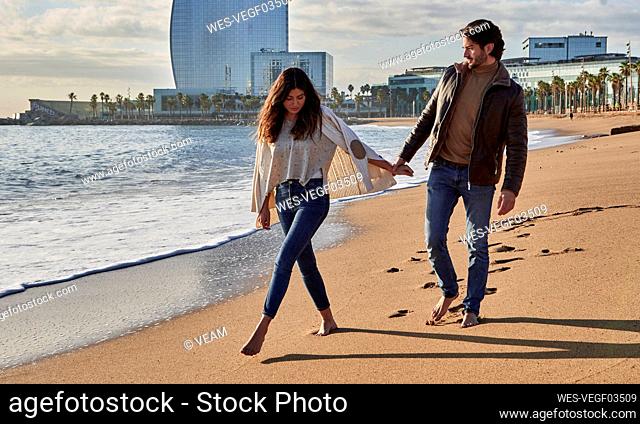 Young man holding hand on woman while walking on beach