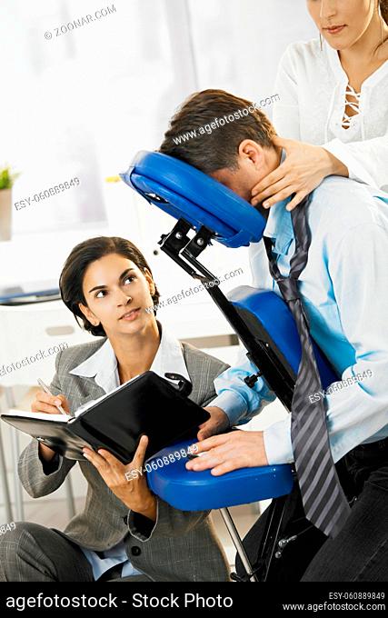 Busy executive working in massage chair, while getting back massage in office