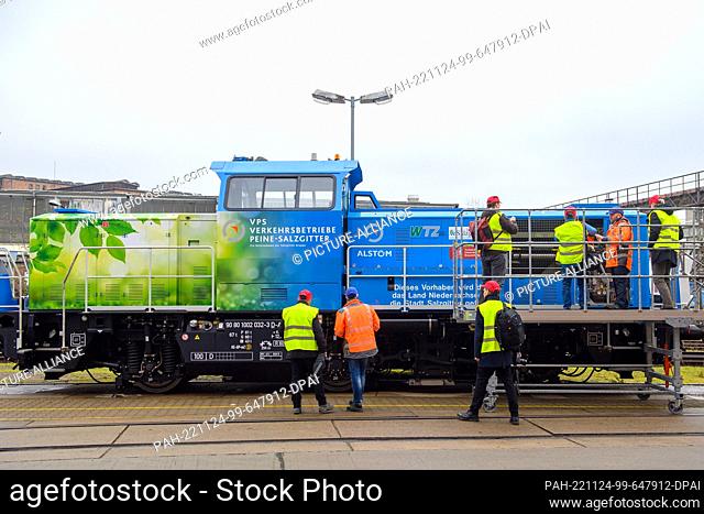 24 November 2022, Saxony-Anhalt, Stendal: Media representatives and Alstom employees stand in front of a hydrogen-powered shunting locomotive