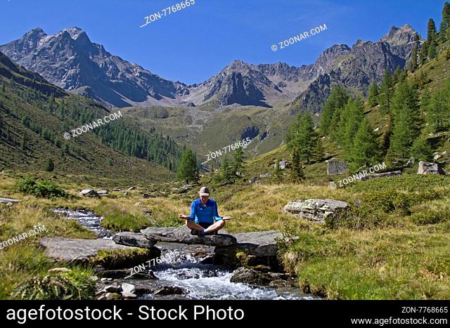 Meditierender Mann auf kleiner Steinbrücke über einem Wildbach