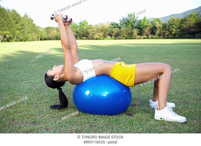 woman excercising with dumbbelll on the gym ball