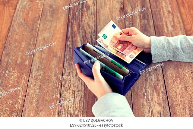 business, finance, saving, banking and people concept - close up of woman hands with wallet and euro money on wooden table