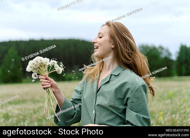 Smiling young woman holding dandelions on field