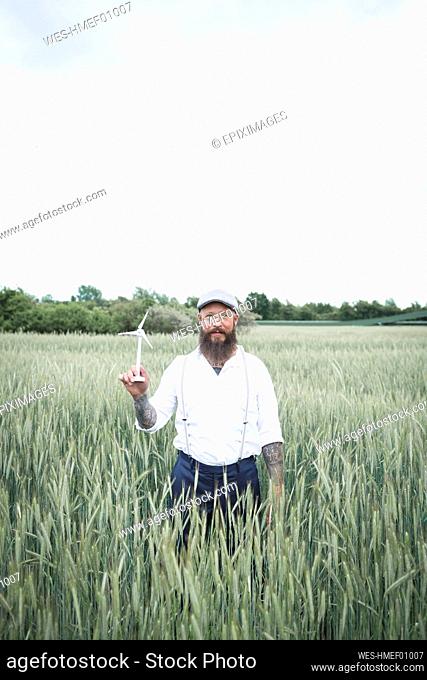Mature man holding small windmill while standing amidst cornfield against sky