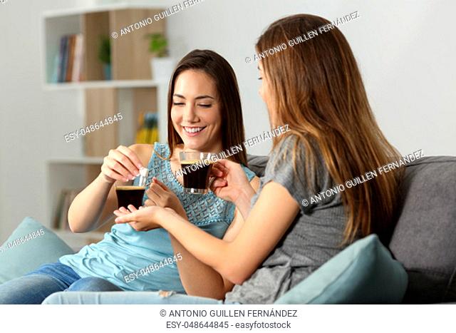 Friend drinking coffee and giving sugar cubes sitting on a couch in the living room at home