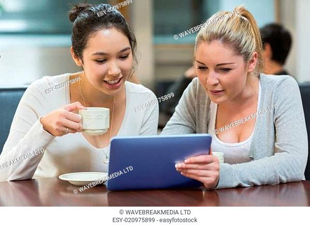 Two students sitting in a coffee shop while drinking coffee and using the tablet pc