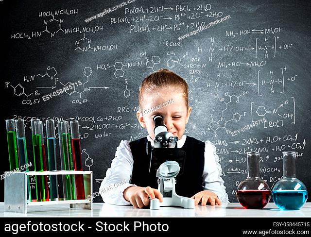 Little girl scientist looking through microscope in classroom at chemistry lesson. School chemical laboratory with glass flasks and test tubes