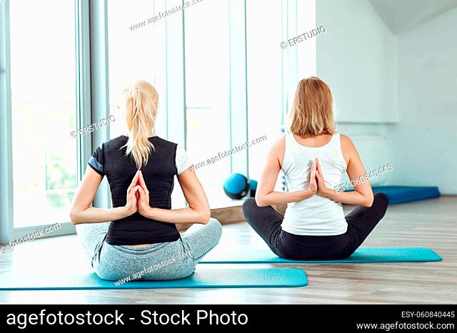 two young women practicing yoga in the gym. girl joining hands behind her back