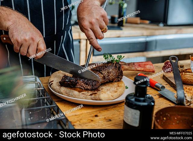 Expertise cutting cooked tomahawk steak in plate while standing in kitchen