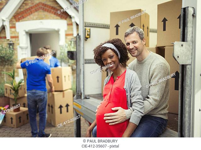 Portrait smiling pregnant couple at moving van outside new house