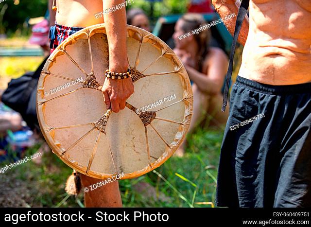 Sacred drums during spiritual singing. A close-up view and side view of man hand holding his sacred native drum, a lot of people in the background