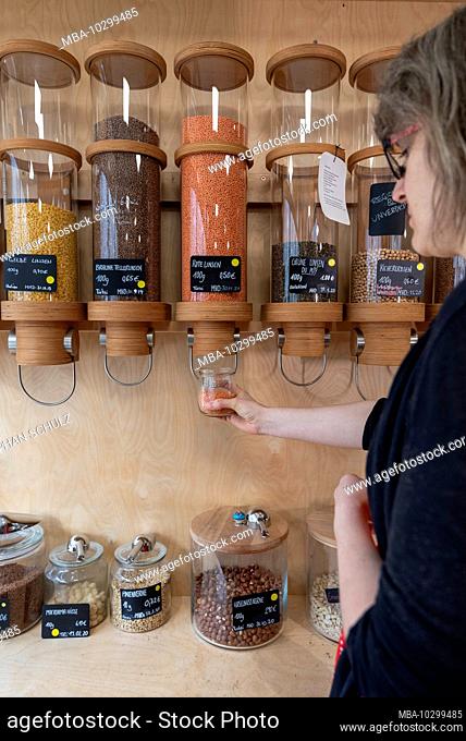 The owner of an unpackaged shop stands on a shelf with filling containers for grain