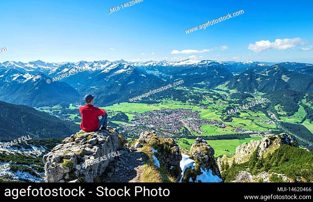 Hiker at the top of Rubihorn enjoys view of Oberstdorf and snow covered mountains on sunny autumn day. Allgäu Alps, Bavaria, Germany, Europe