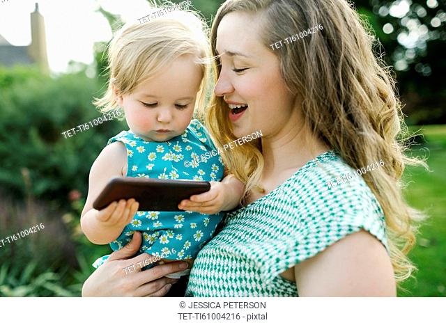Mother carrying daughter (12-17 months), daughter playing on smartphone
